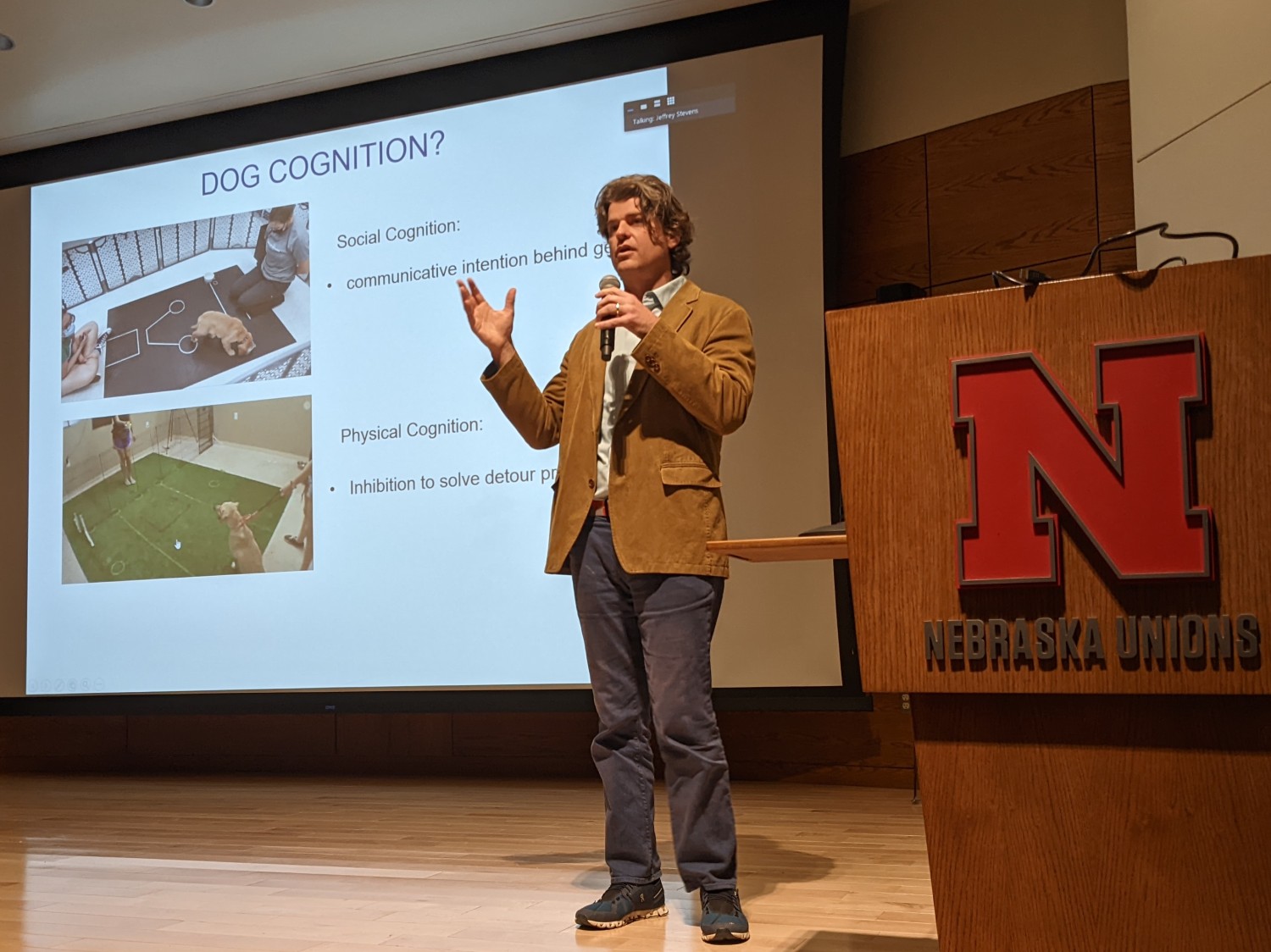 Dr. Brian Hare standing in front of his presentation slides